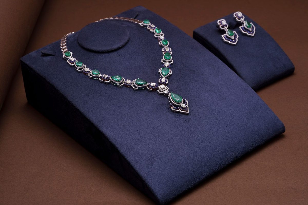 Emerald and diamond necklace with matching earrings on navy display stands