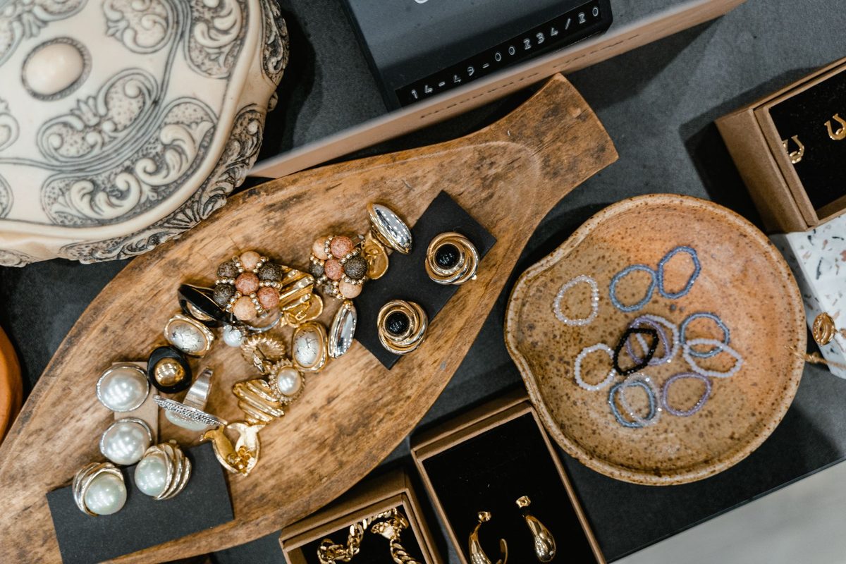 Assorted rings on a wooden tray beside beaded bracelets in a ceramic dish and boxed jewelry