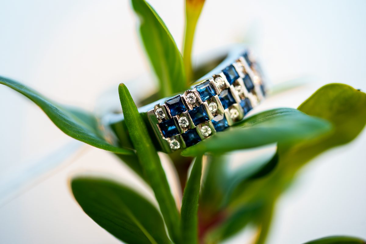 Ring with rectangular blue stones and round clear stones resting among green leaves