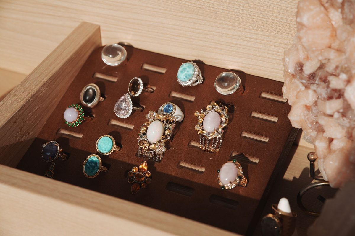 Gemstone rings with white, blue, green and clear stones arranged in a brown-lined wooden display box