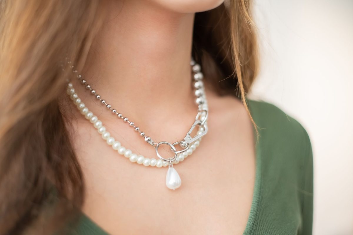 A white bead necklace with a drop pendant layered with a silver-coloured chain over a green top